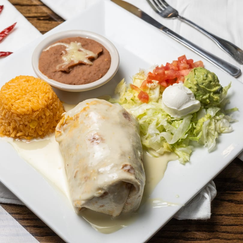 Mi Casita's burrito covered in white sauce, with rice, refried beans, and salad on a white plate.