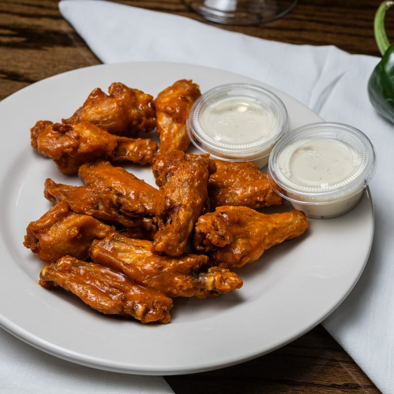 Mi Casita's buffalo wings, coated in a vibrant orange sauce, served with two dipping cups.