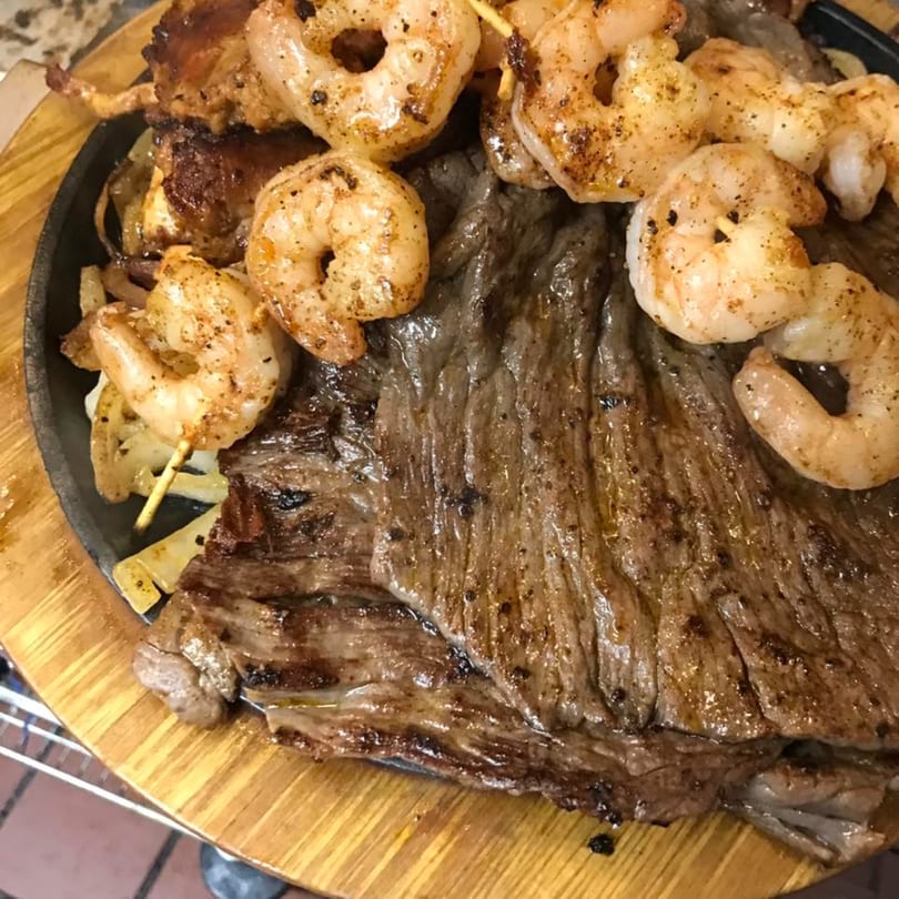Sizzling Mi Casita fajitas with grilled steak, shrimp skewers, and onions on a wooden platter.