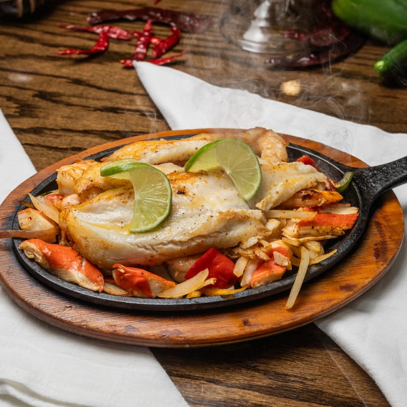 Steaming Mi Casita fajitas with chicken, shrimp, vegetables, and lime on a sizzling cast iron plate.