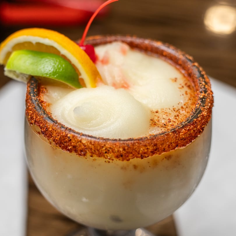 Frozen margarita in a chili-rimmed glass, garnished with orange, lime, and a cherry.