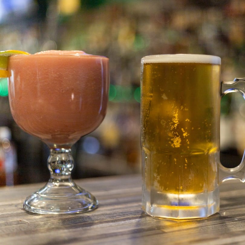 A frozen strawberry margarita and a mug of beer on a wooden bar top at Mi Casita.
